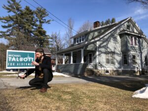 Michael Talbott crouched in front of a home, planting a "Talbott for alderman" campaign sign.